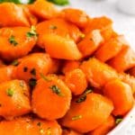 A white bowl of Brown Sugar Glazed Carrots garnished with parsley.