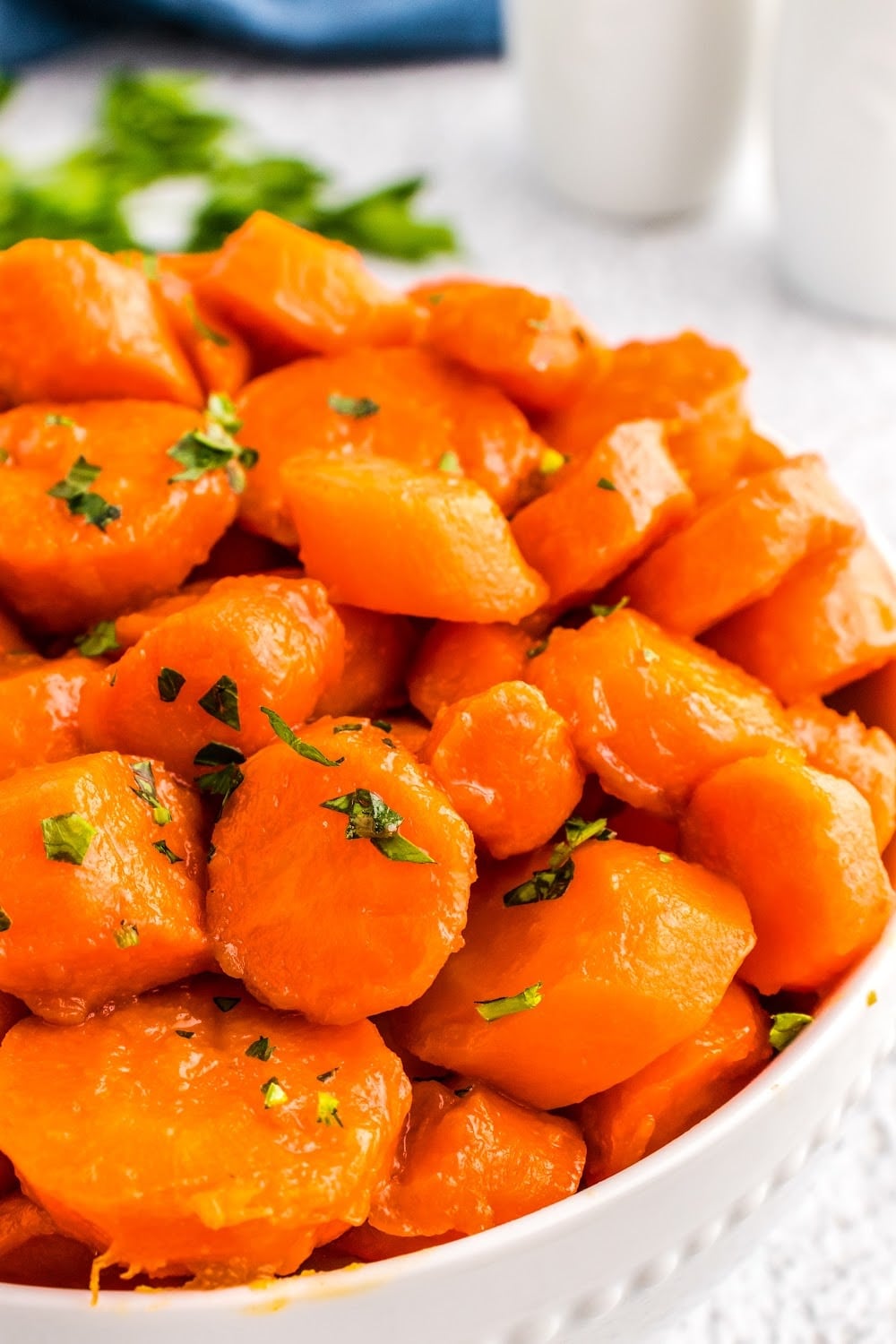 A white bowl of Brown Sugar Glazed Carrots garnished with parsley. 