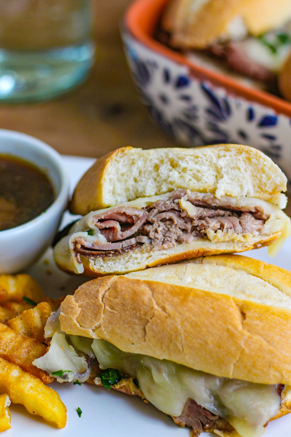 French Dip Sandwich cut in half next to a white bowl of au jus on white plate