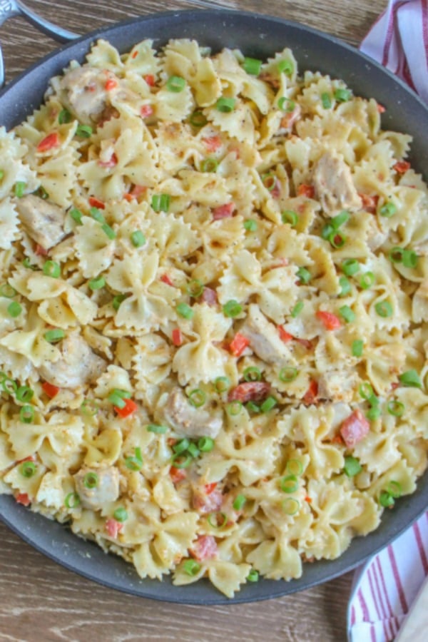 Cajun Chicken Pasta Recipe in large skillet garnished with scallions and cracked black pepper on wooden back ground 