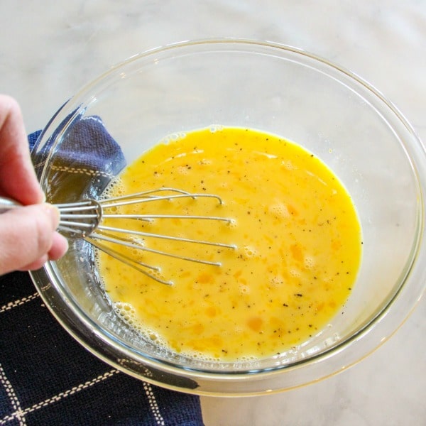 Eggs, milk, salt and pepper whisked together in a clear glass bowl 