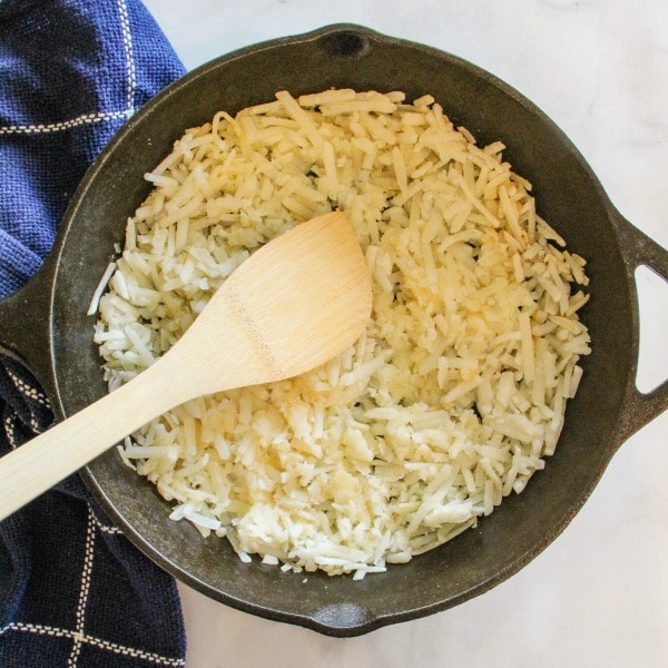 Sautéed hash browns in a cast iron skillet with wood spatula 