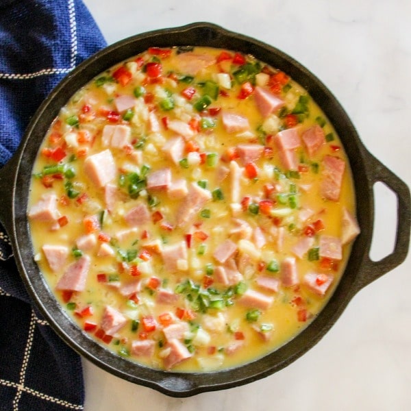 Egg and ham mixture poured over sautéed hash browns in a cast iron skillet 