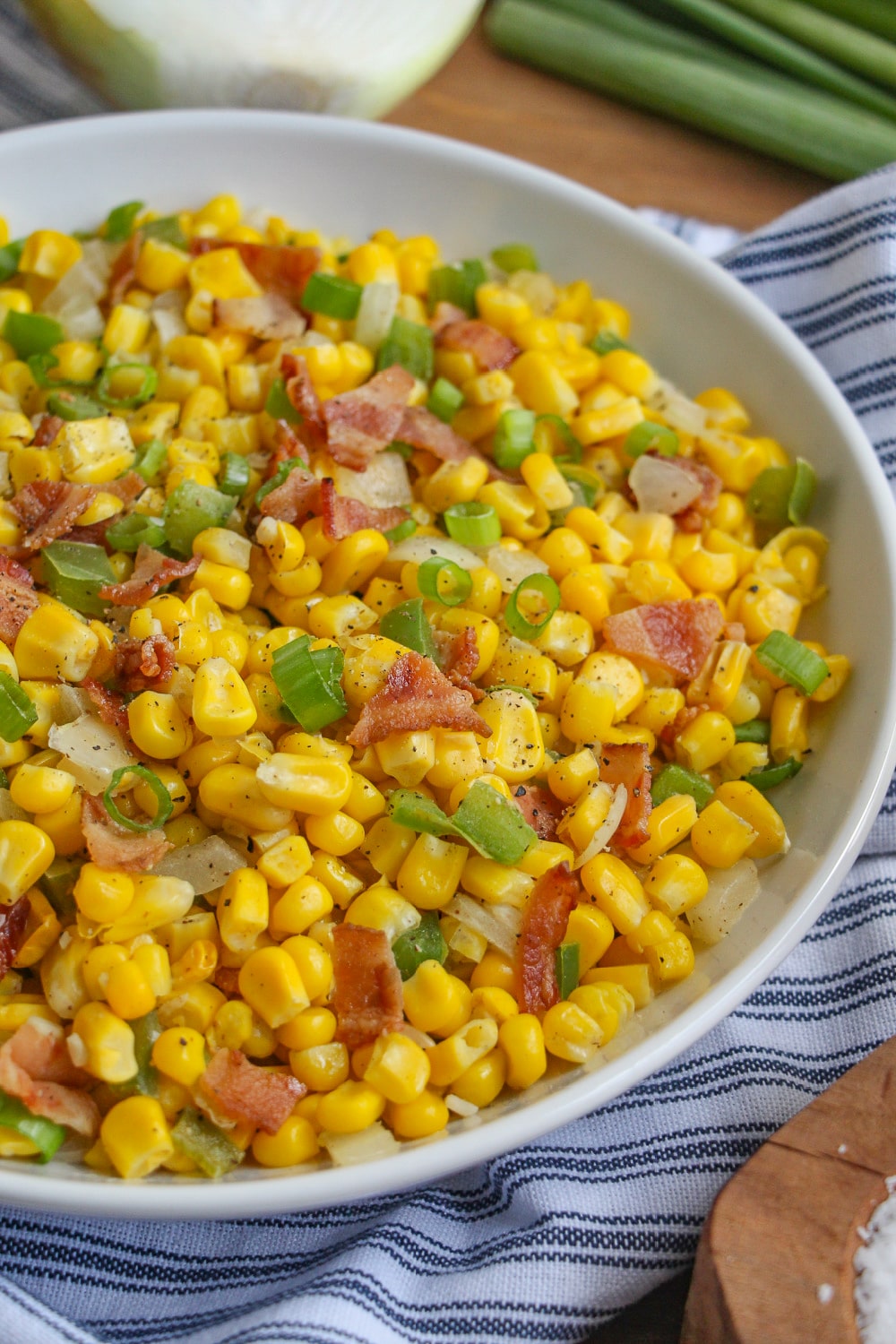Fried corn, onions, bell peppers and bacon in a white bowl on a wood cutting board.