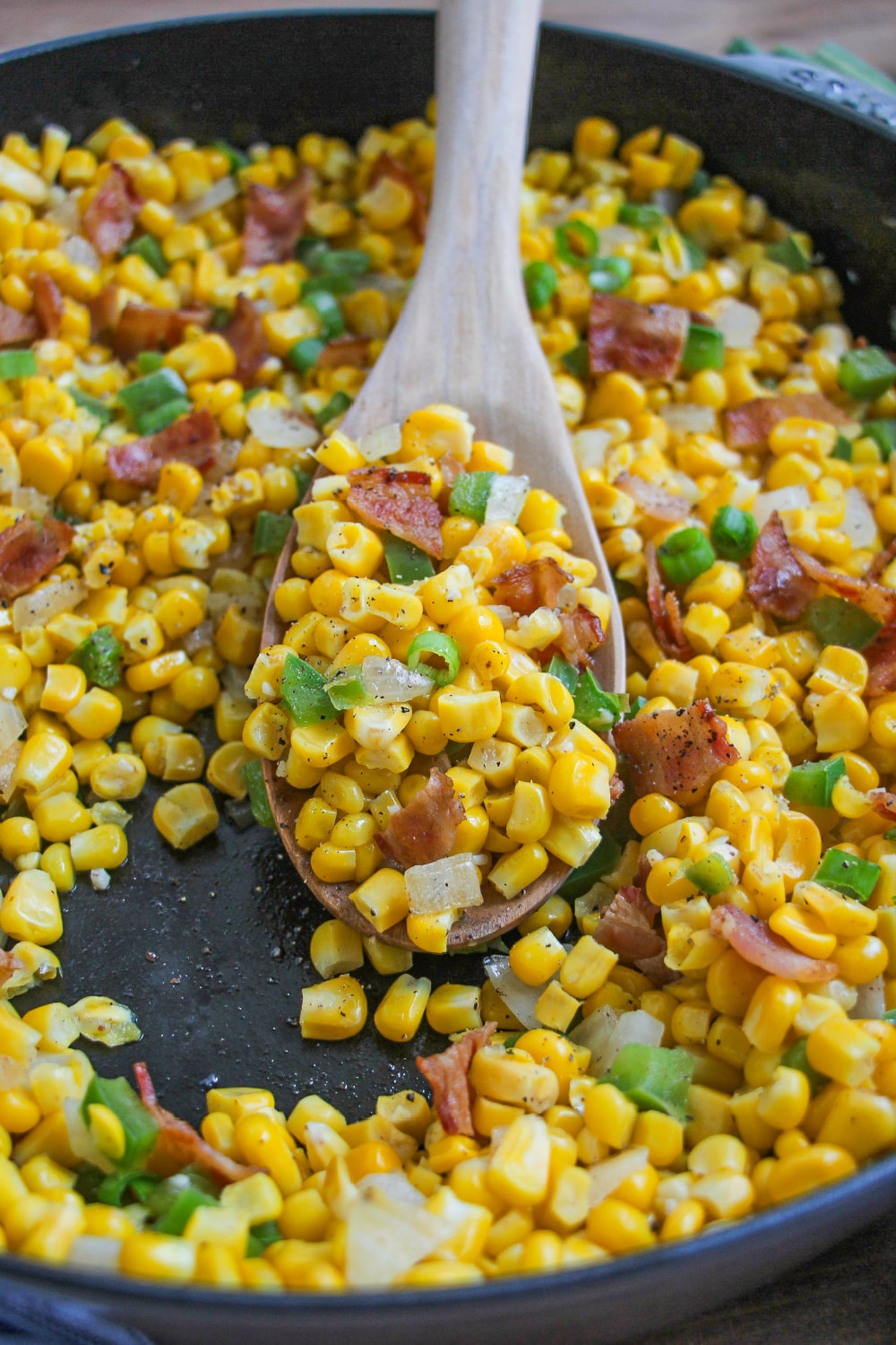 A wooden spoon filled with fried corn rest in a skillet.