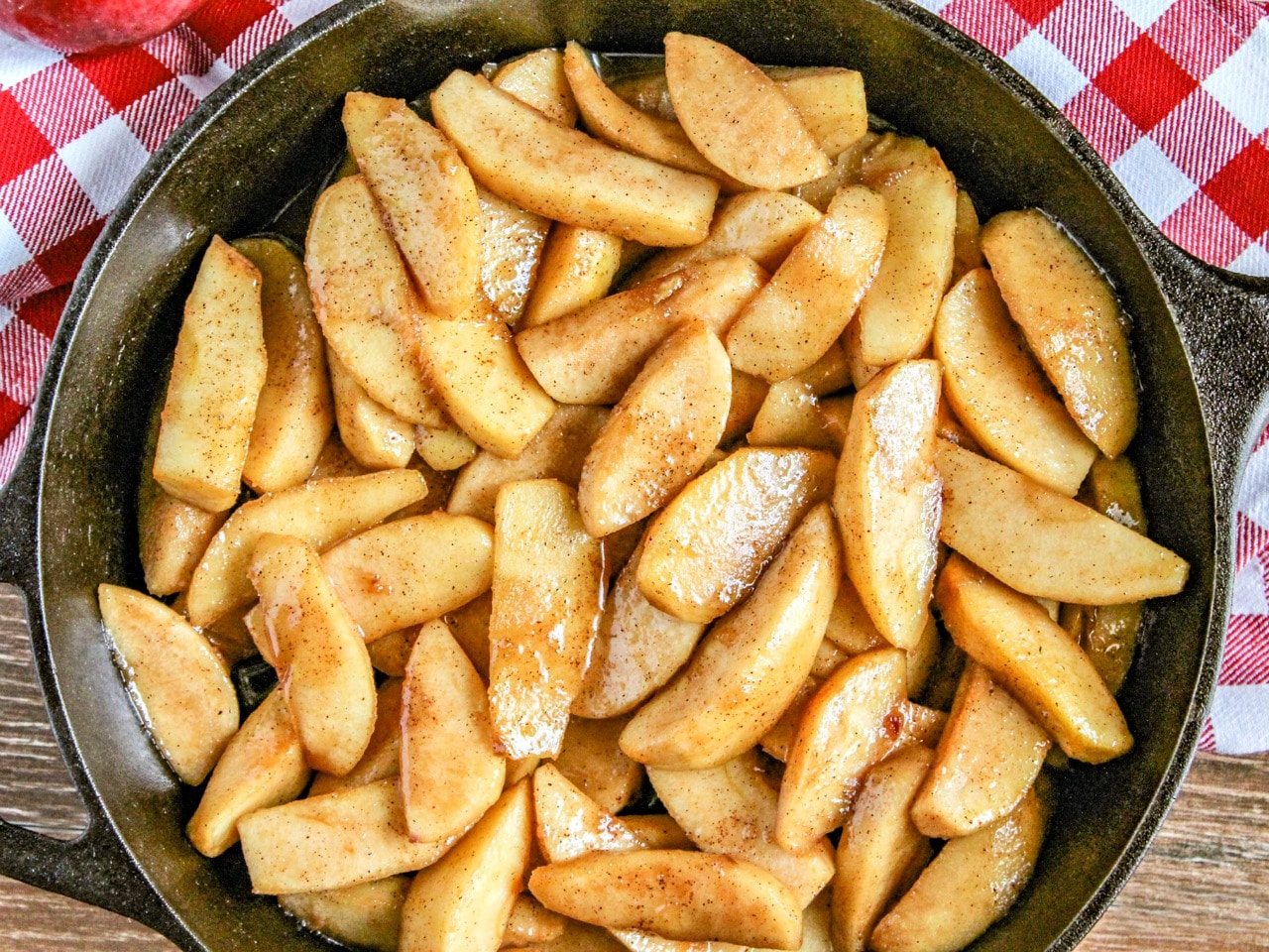 Southern Style Fried Apples  in black cast iron skillet with red and white checked napkin on wood cutting board 