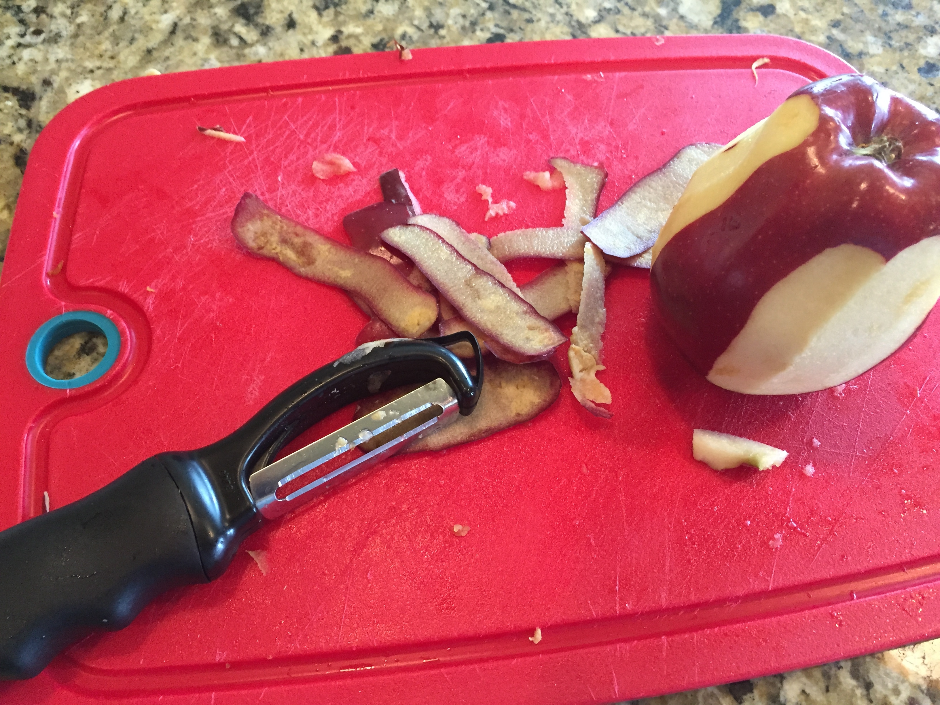 apple being peeled on red cutting board 