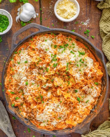 A cast iron skillet filled with lasagna garnished with parmesan and parsley.