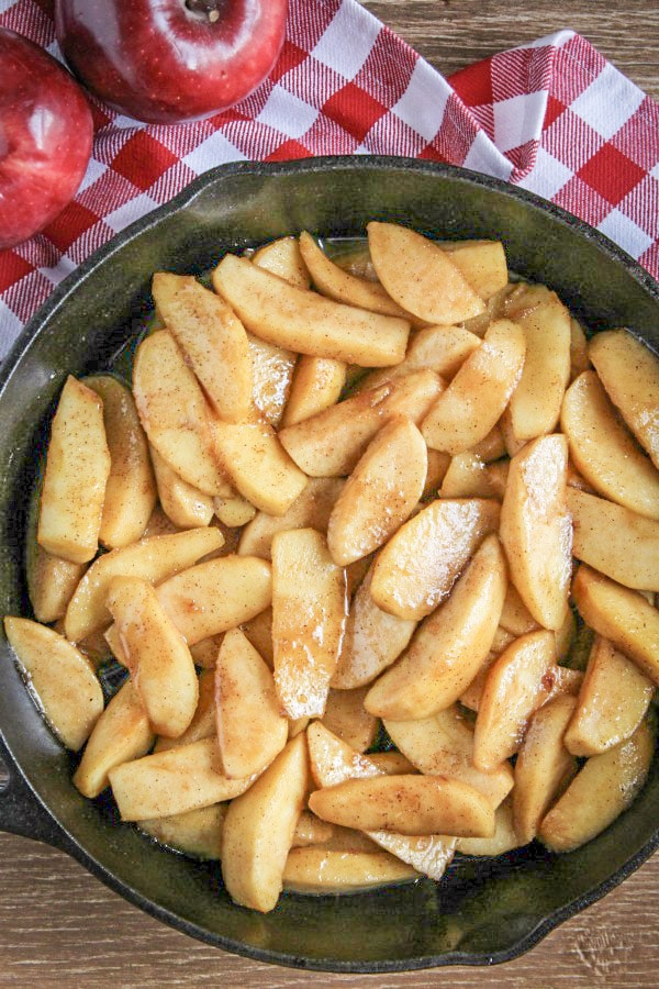 Fried Apples in a black cast iron skillet on red and white check napkin and red apples 
