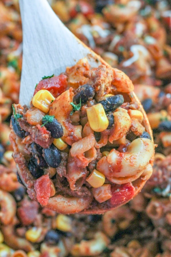 A wooden spoonful of Taco Mac 'n Cheese with elbow noodles, black beans, corn kernels, and diced tomatoes and ground beef. https://newsouthcharm.com/skillet-taco-mac-cheese/