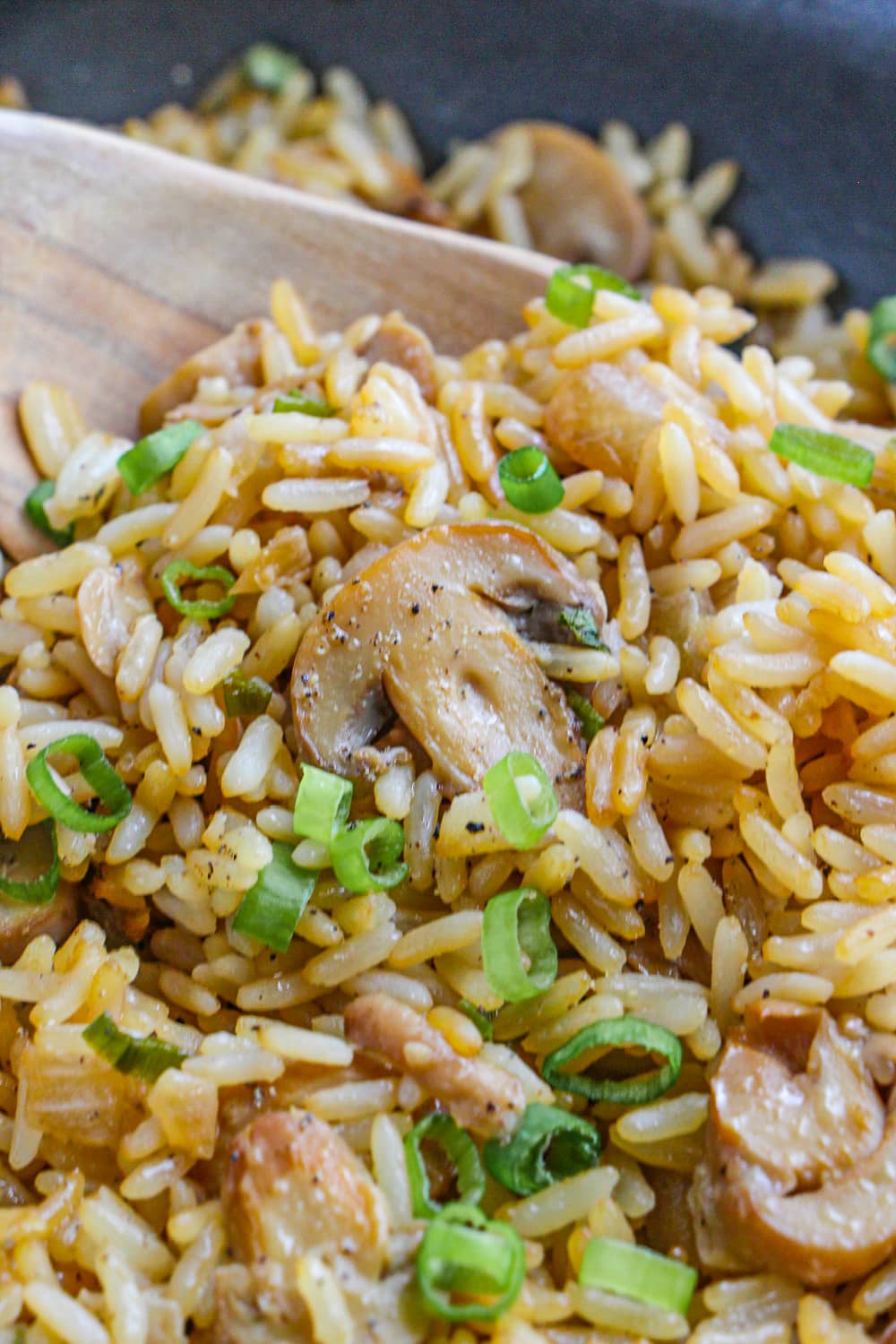 A close up photo of fried rice with mushroom and sliced green onion ins a wooden spoon.