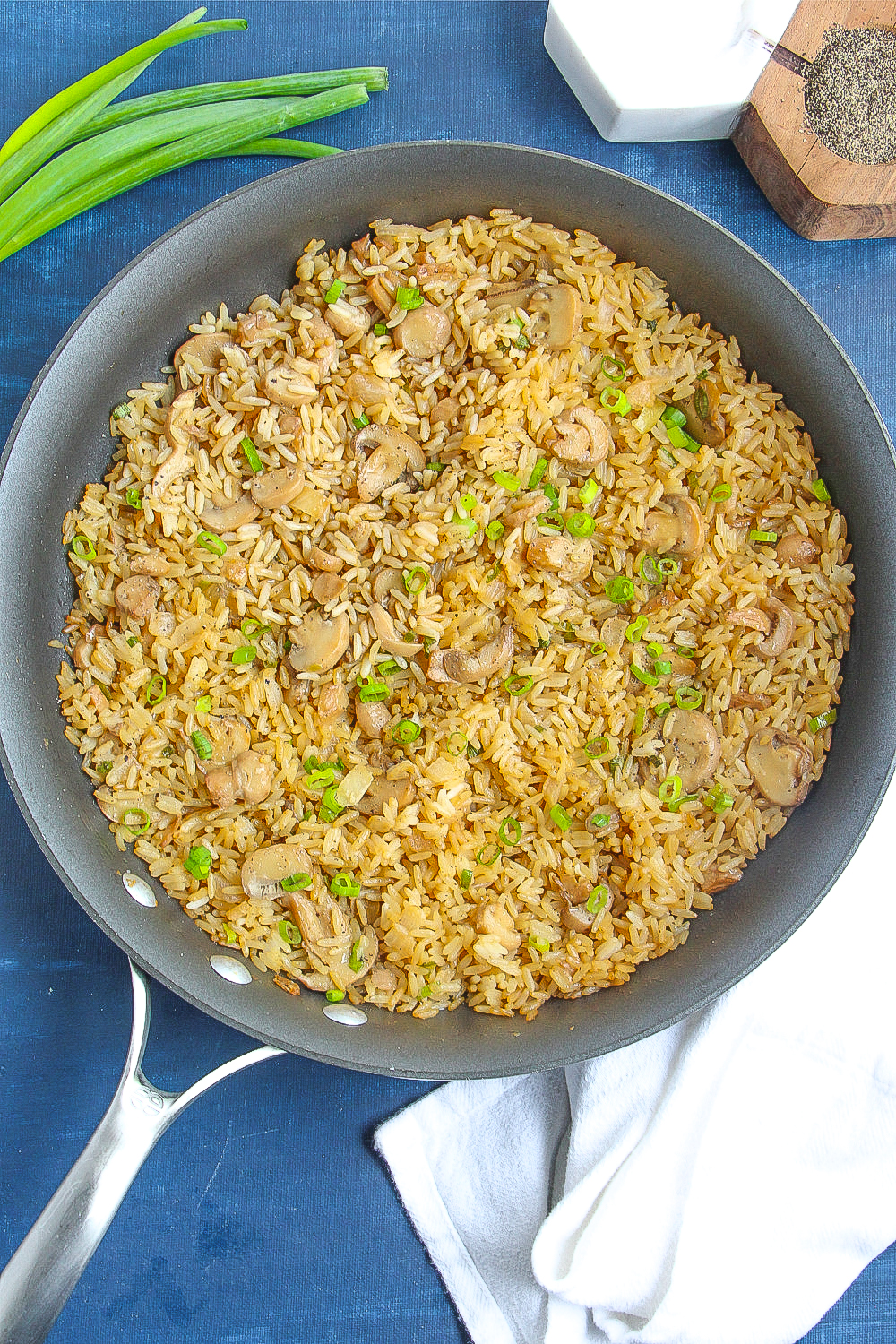 A large skillet with Mushroom Fried Rice rests on a blue backdrop.