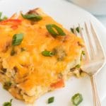 A single slice of breakfast casserole on a white plate garnished with sliced scallions.