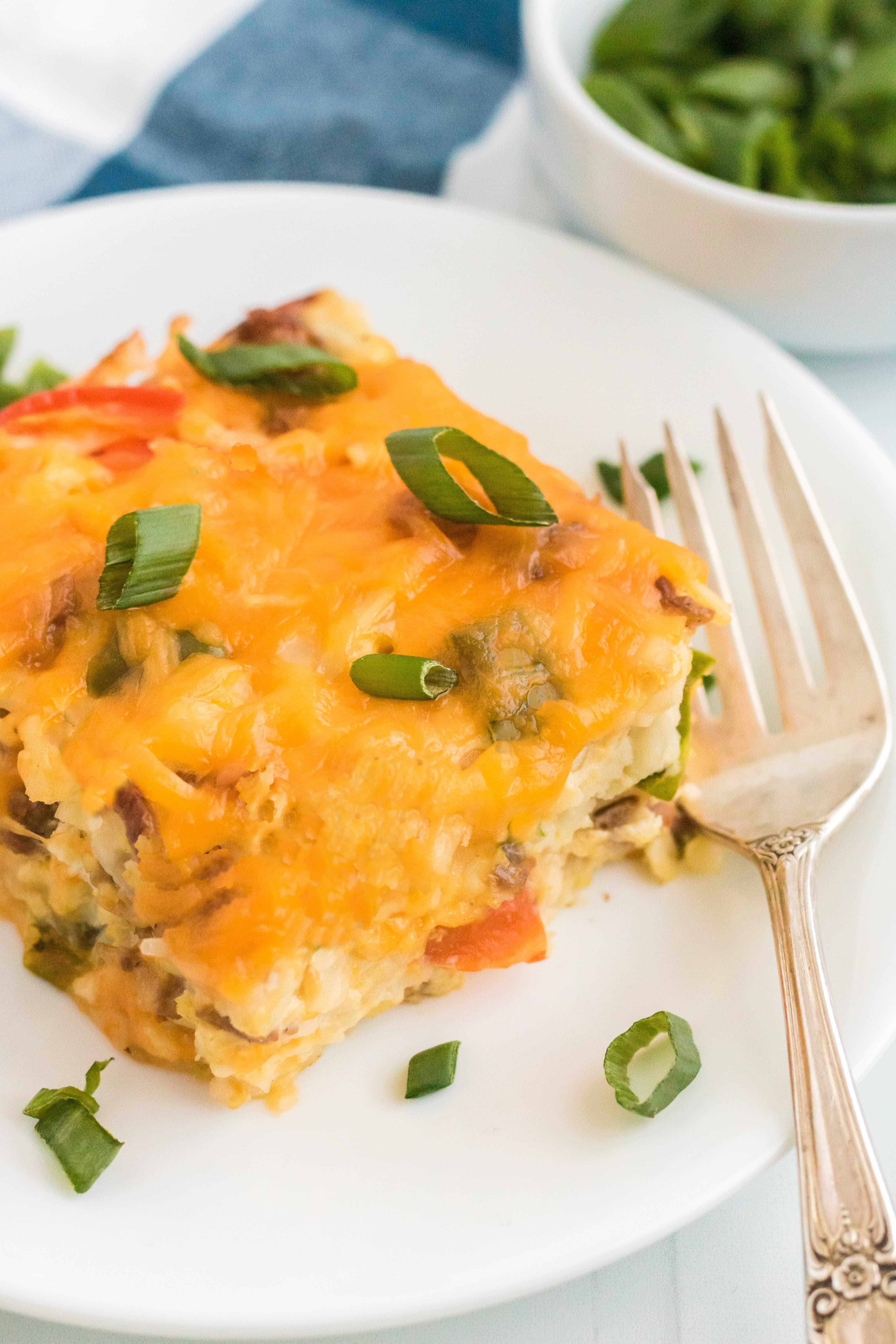 A single slice of breakfast casserole on a white plate garnished with sliced scallions. 