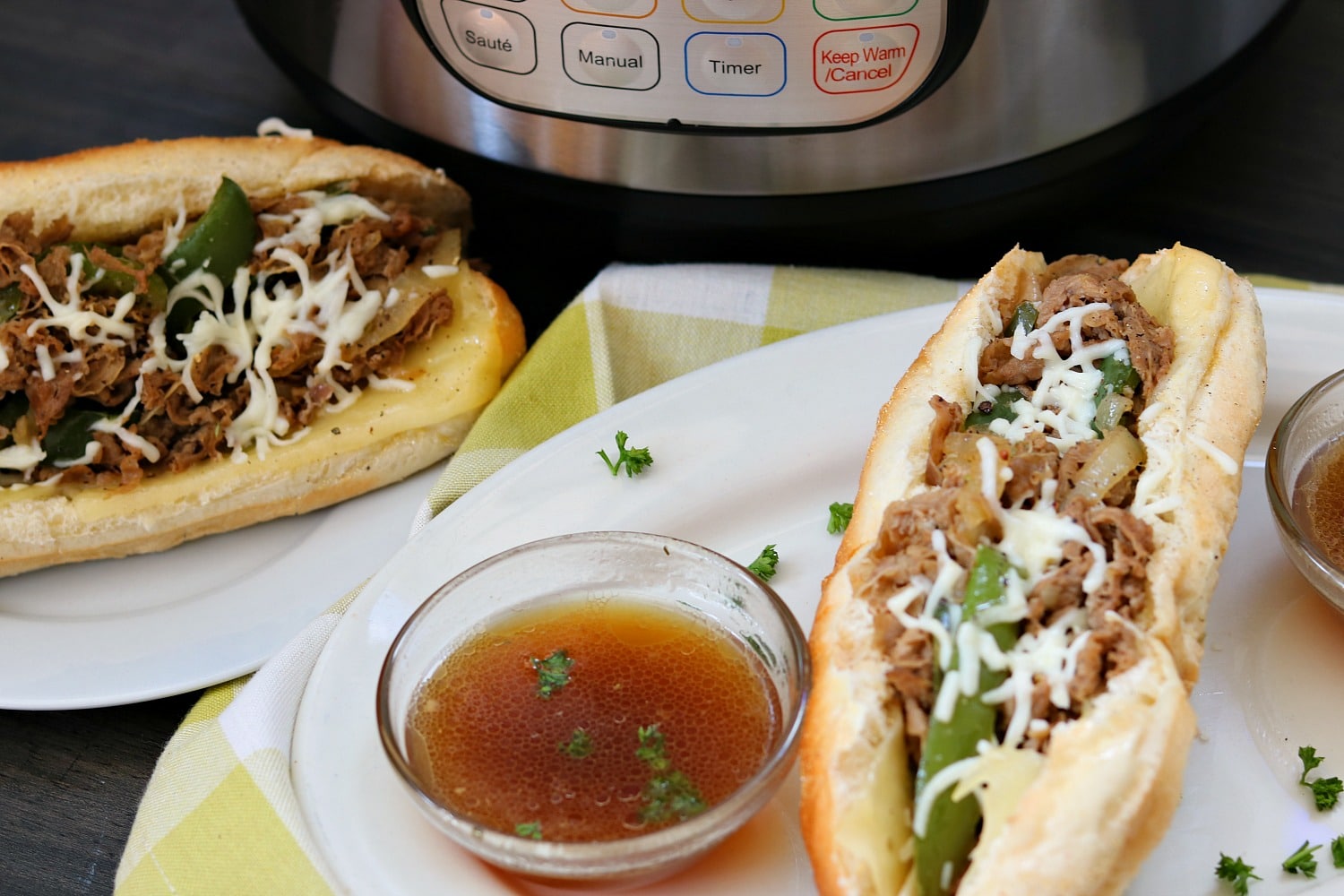 instant pot steak sandwiches on white plates with au jus in clear bowls on green and white napkin with Instant Pot in background