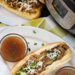 Steak sandwiches on white plates in front of an instant pot.