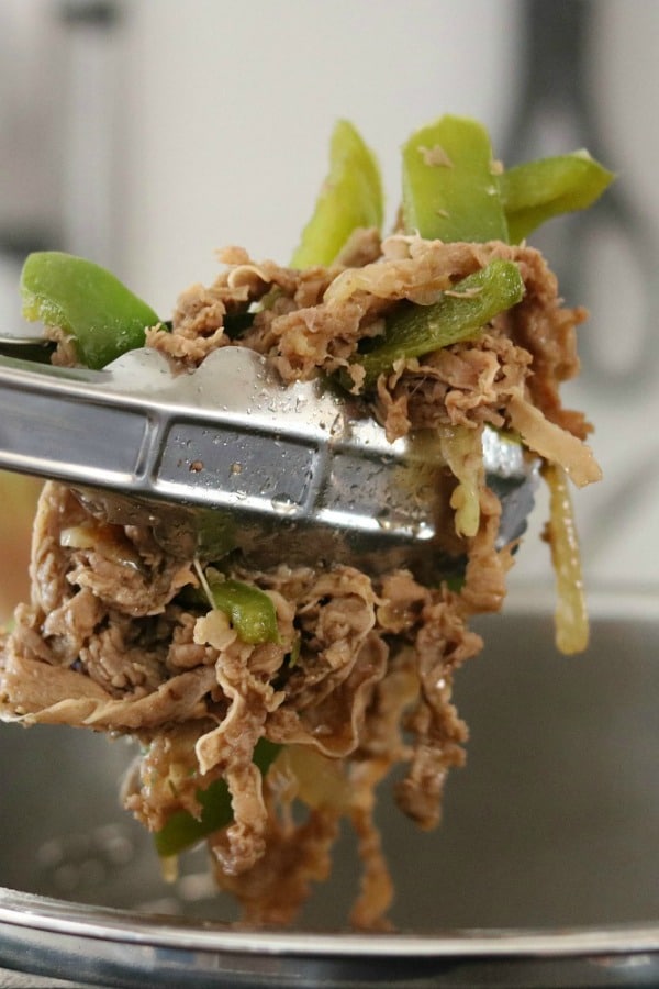 shredded beef and bell peppers in tongs being removed from Instant Pot 