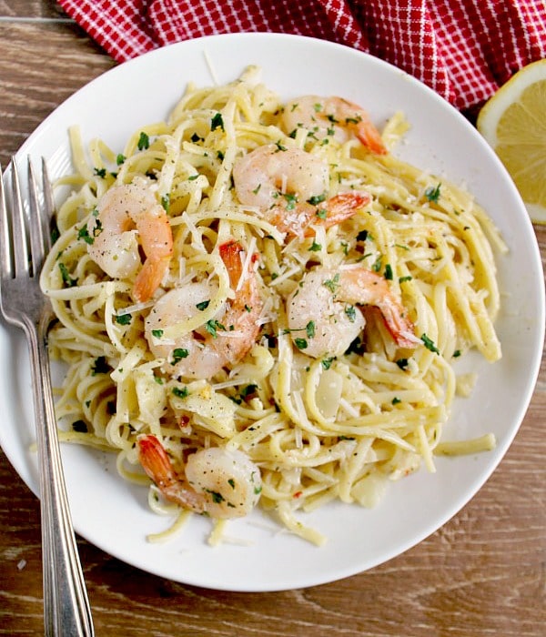 Shrimp pasta on a white plate with fork garnished with parmesan cheese and parsley 