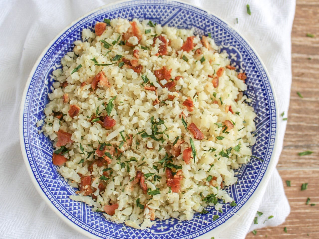 blue and white bowl of cauliflower rice resting on a white dish towel on wooden background 