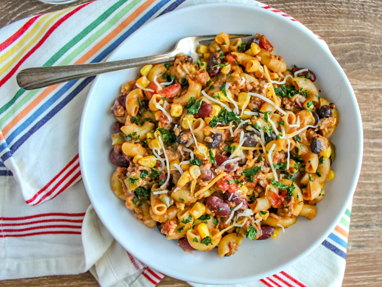 Instant Pot Taco Pasta in a white bowl with fork on multicolored striped napkin.