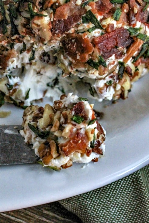 A bite of cheeseball scooped onto a knife laying on white platter with remainder of cheeseball behind 