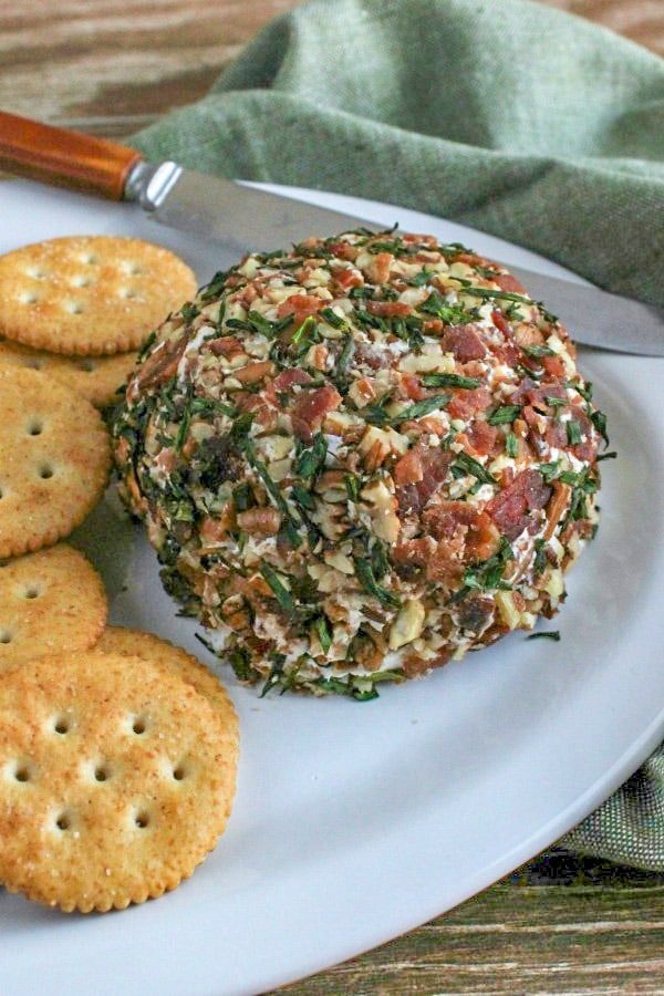 Bacon and Chive Cheeseball with crackers on a white platter with knife and green napkin in background