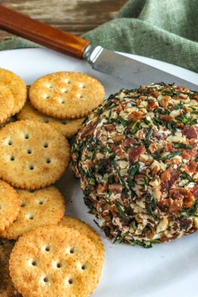 Bacon and Chive Cheeseball with crackers on a white platter with knife and green napkin in background