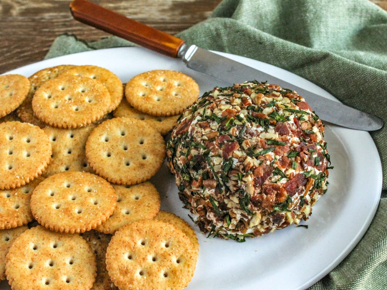 Bacon and Chive Cheeseball with crackers and knife on a white platter 