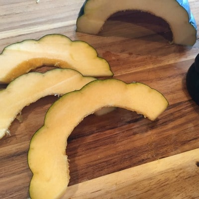 acorn squash on cutting board seeds removed and sliced into moon shapes