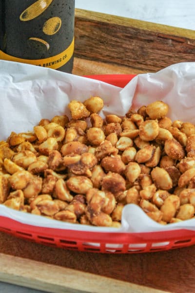 Slow Cooker Sweet and Spicy peanuts in a red plastic basket with white parchment with two bottles of beer on a wooden tray