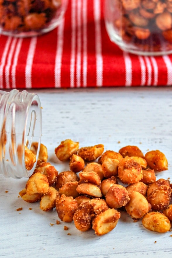 slow cooker candied peanuts spilling out of a glass bottle onto a white background 