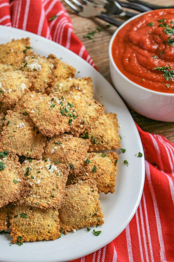 Fried Ravioli  on a white platter on a red and white stripe towel with a bowl of marinara sauce for dipped to the right