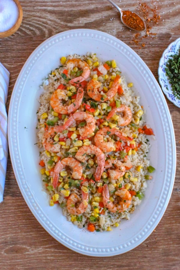 Cajun Shrimp recipe with mixed vegetables over rice served on a white platter and garnished with black pepper and parsley 
