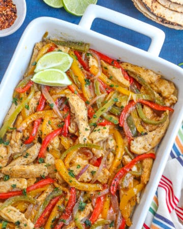 Cooked chicken, onion and peppers in a white baking dish.