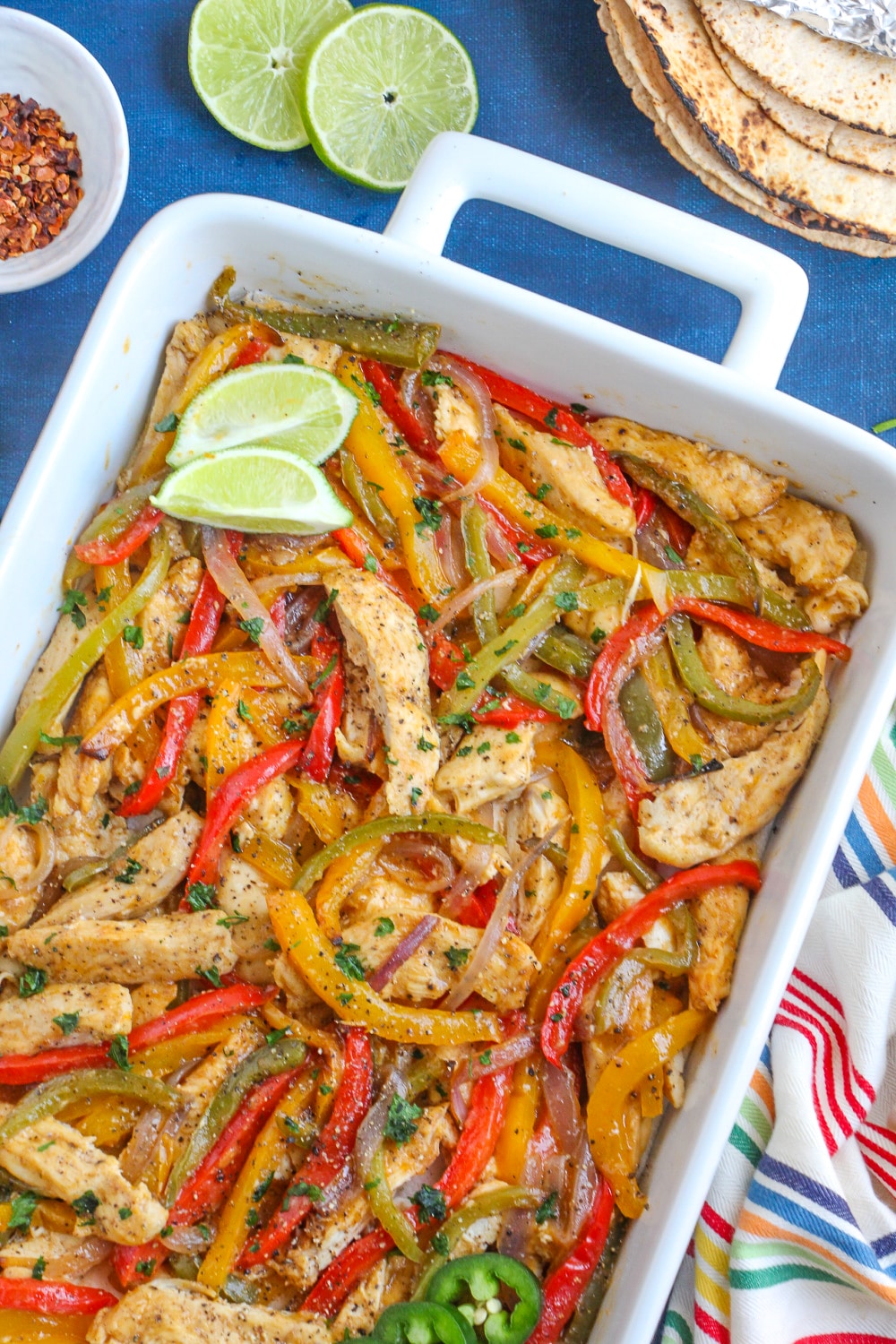 Cooked chicken, onion and peppers in a white baking dish.