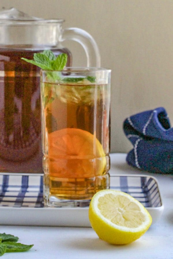 Glass of iced tea garnished with mint sitting on blue and white tray. 