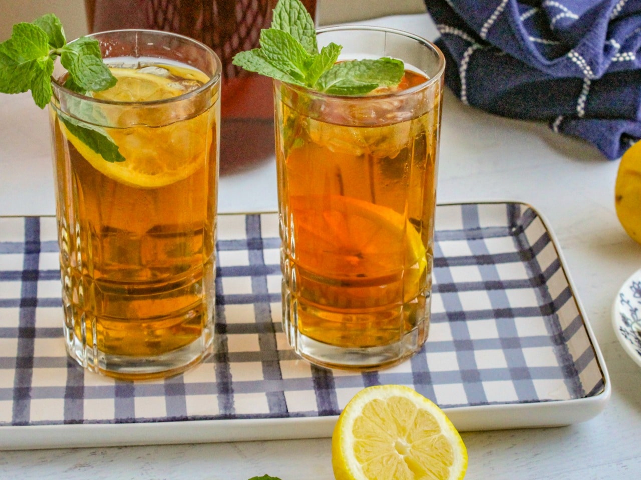 Two glasses of iced tea garnished with mint and lemon sitting on blue and white tray. 