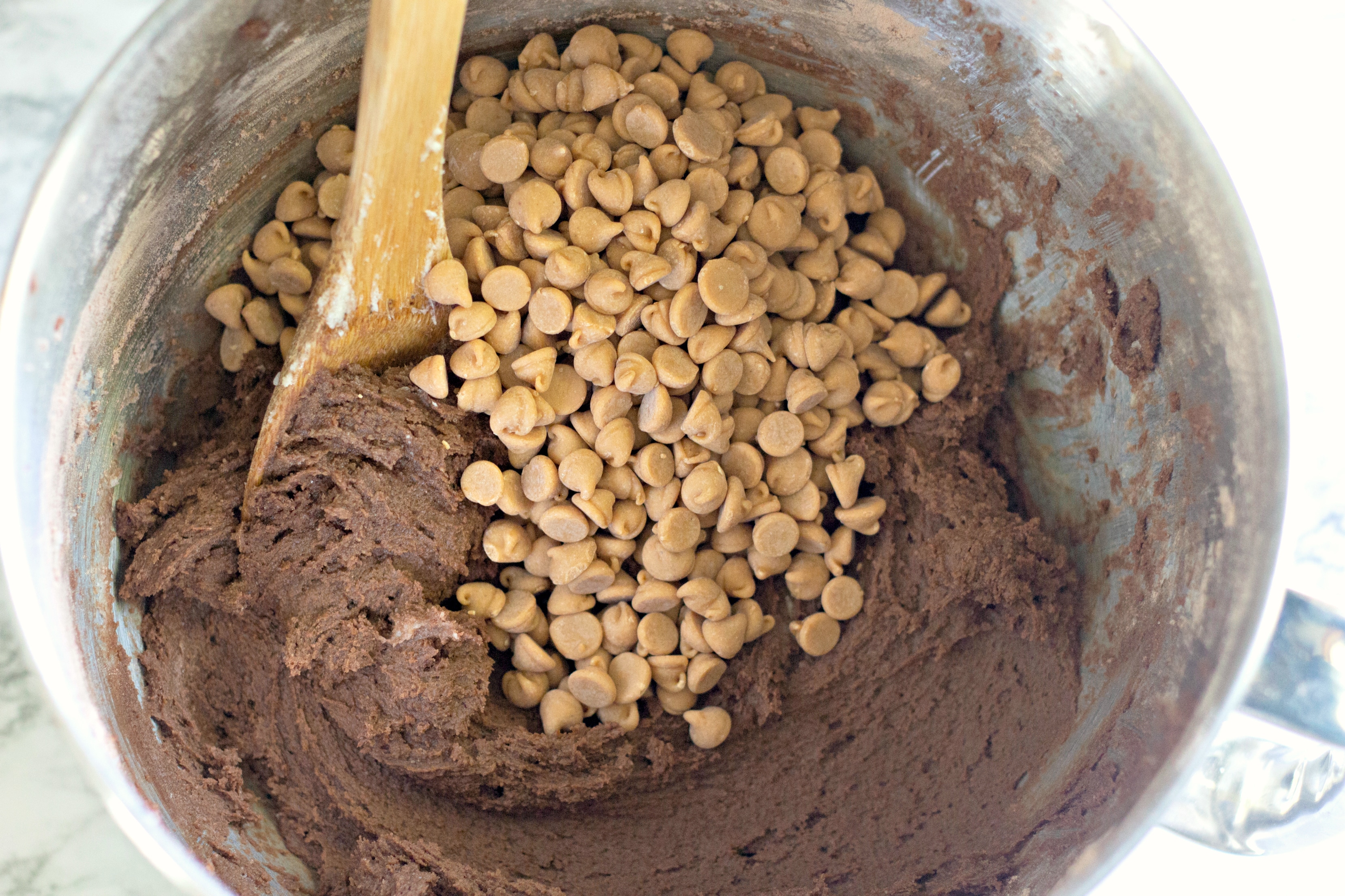 peanut butter chips with chocolate cookie dough in larger metal mixing bowl with wooden spoon