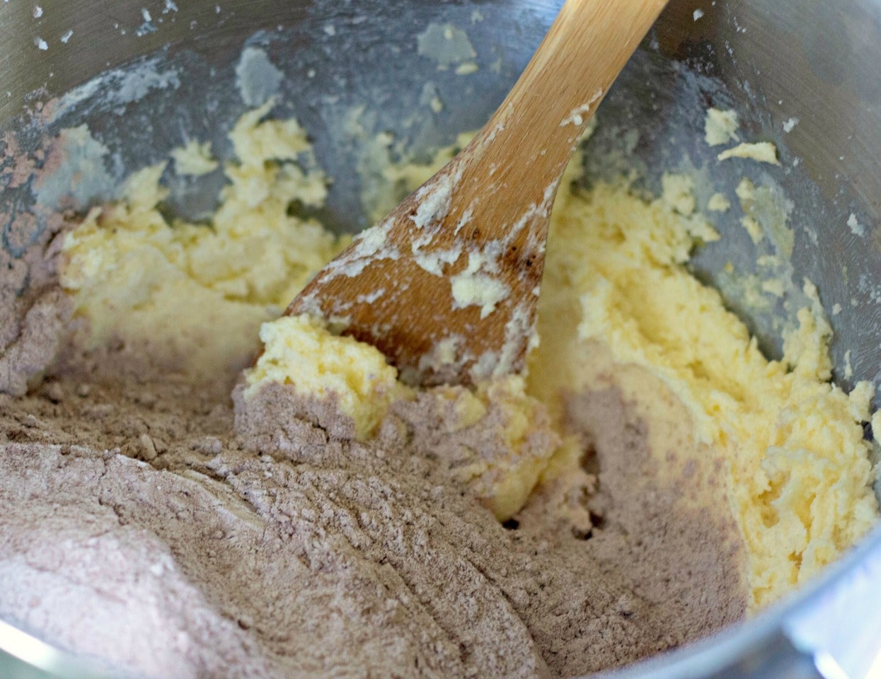 dry mixed ingredients poured into metal mixing bowl with creamed butter and sugar to be combined with wooden spoon