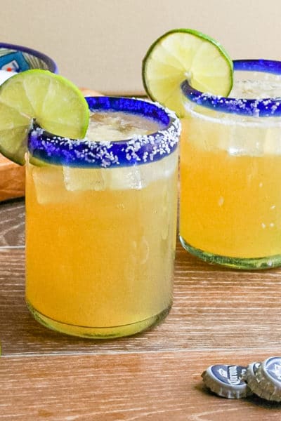 Two Beer Margaritas in a clear glass with salt lined rim and garnished with a slices of lime.