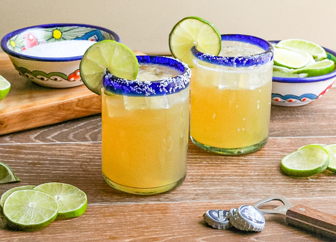 Two Beer Margaritas in a clear glass with salt lined rim and garnished with a slices of lime.