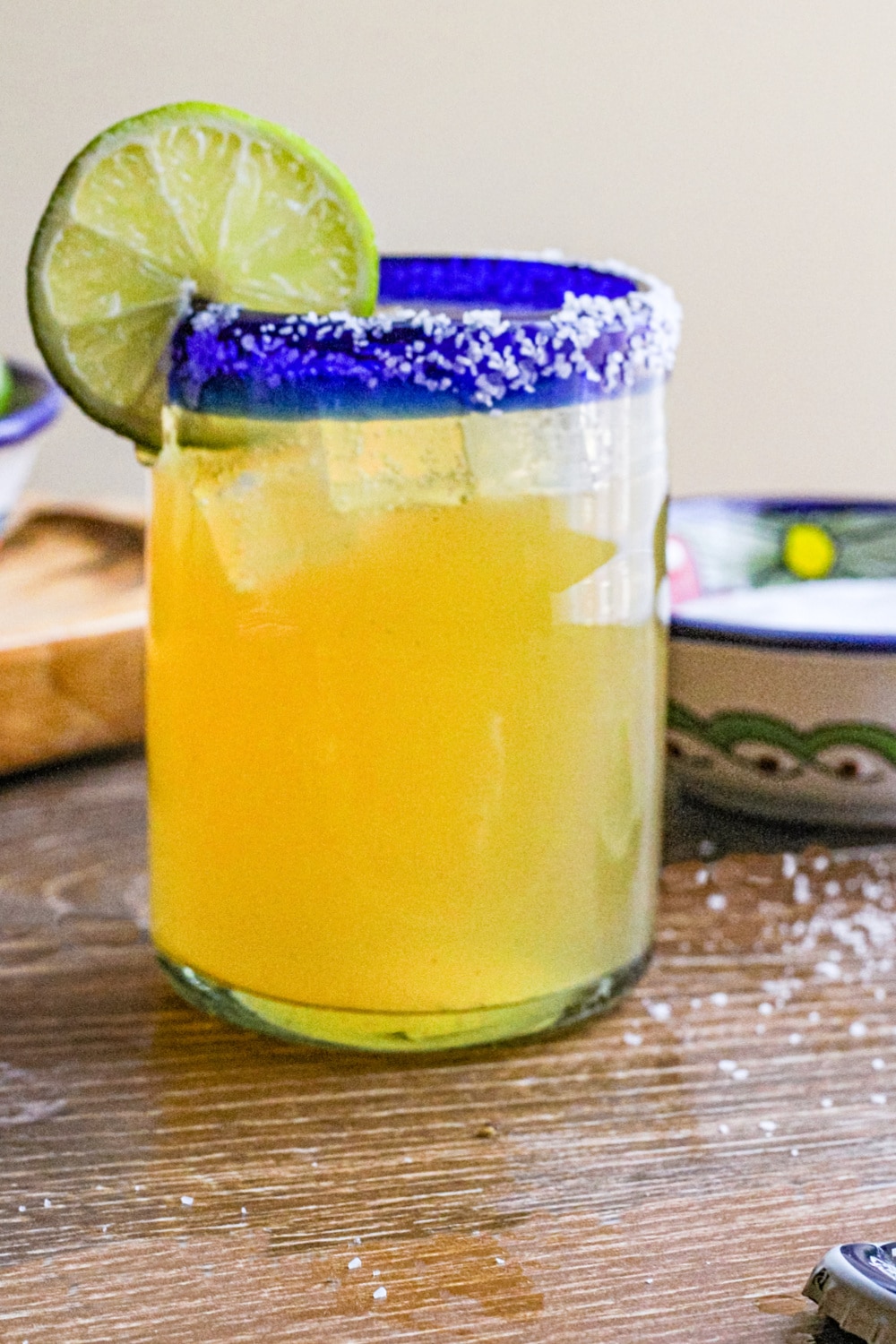 Beer margarita in a clear glass with salt lined rim and garnished with a slice of lime.