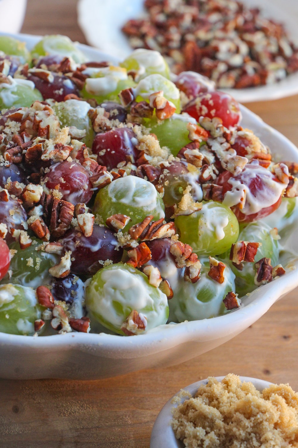 Grape salad in a white serving bowl resting on a. wood cutting board.