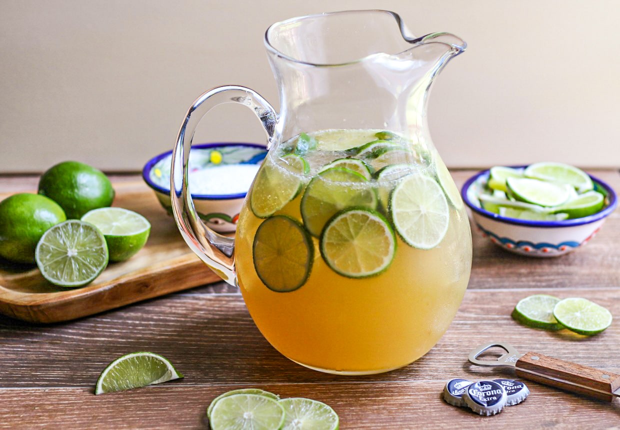 a pitcher of Beer Margaritas with limes on a wood table. 
