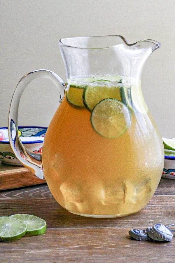 clear pitcher filled with beer margarita garnished with lime on the rocks