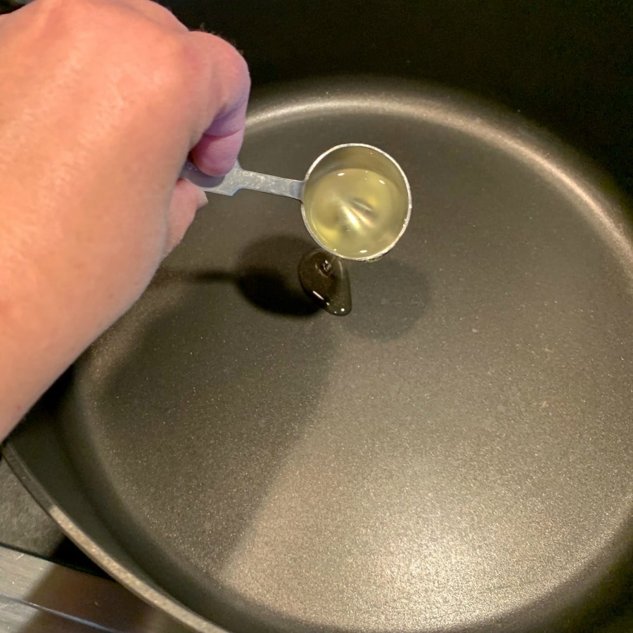 Stovetop popcorn process photo of oil being poured into the bottom of a skillet. 