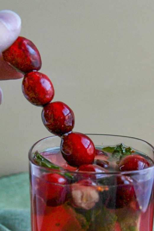 Fresh cranberries on skewer being placed in a glass of Cranberry Mojitos