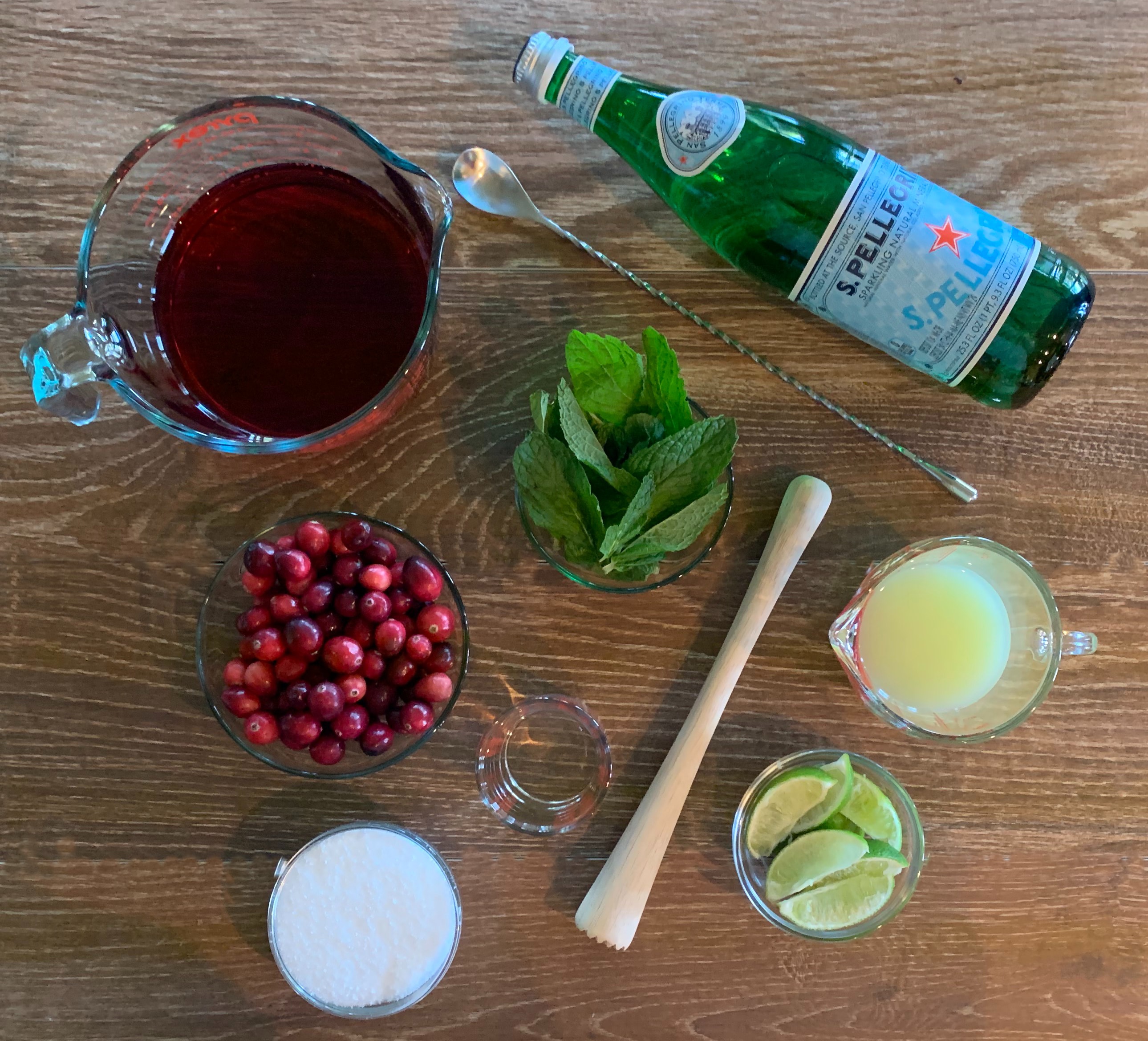 Cranberry Mojitos ingredients: cranberry juice, fresh cranberries, mint, lime juice and lime slices with a bar spoon and muddler