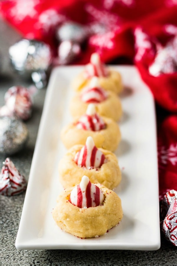 Candy Cane Blossom Cookies on a white platter with red towel and Hershey's kiss candies in background 