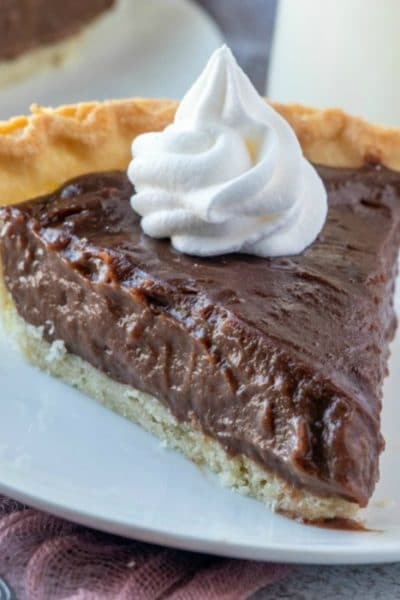 Chocolate pie topped with whipped cream on a white plate.